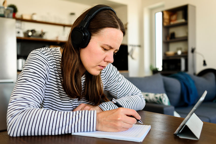 woman with headphones, writing on a piece of paper
